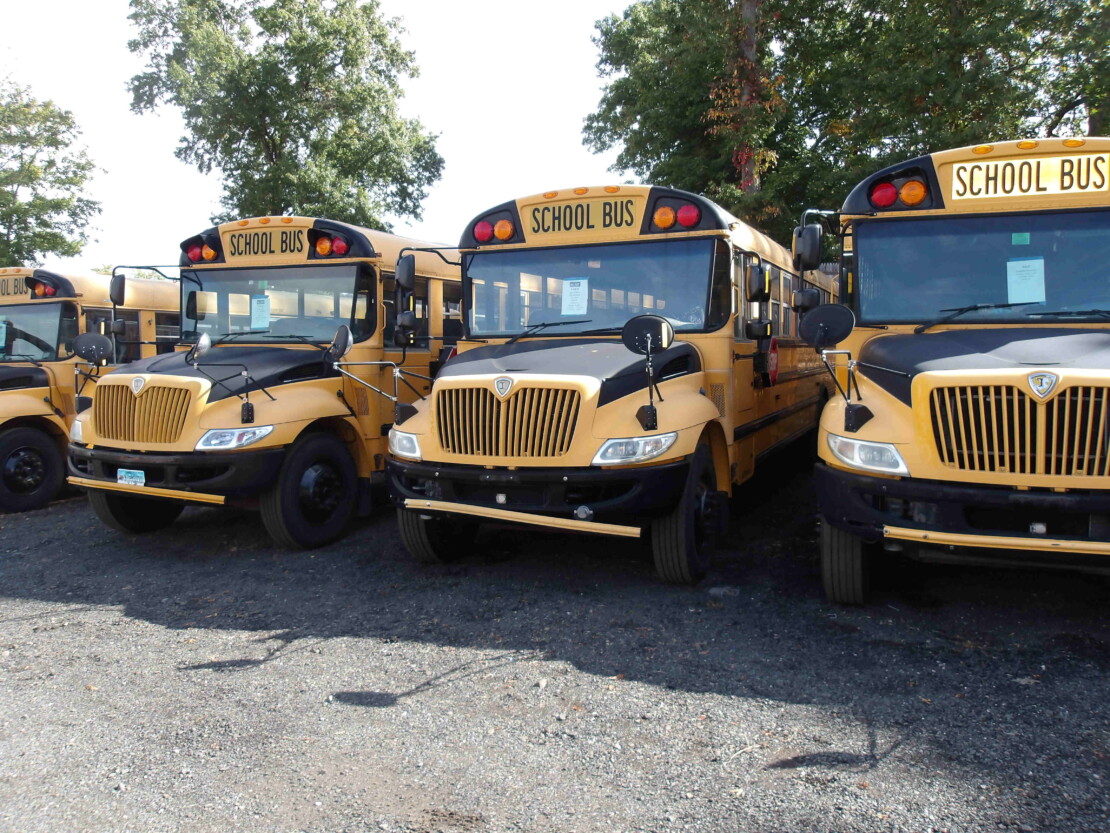 line up of 4 yellow school buses on gravel